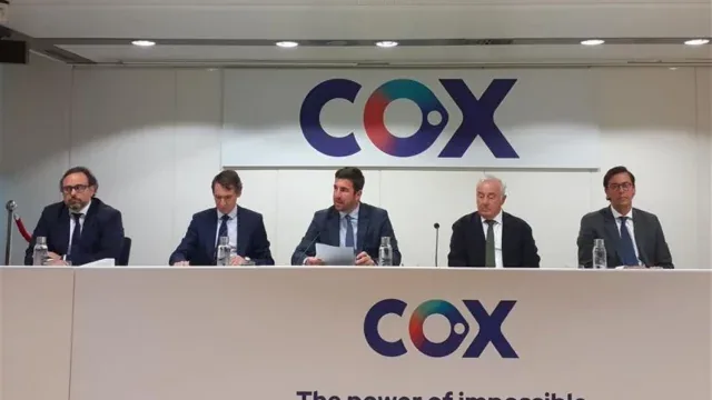 Cinco ejecutivos en traje sentados en una mesa blanca durante una conferencia de prensa. Detrás, el logo 'COX' y botellas de agua.