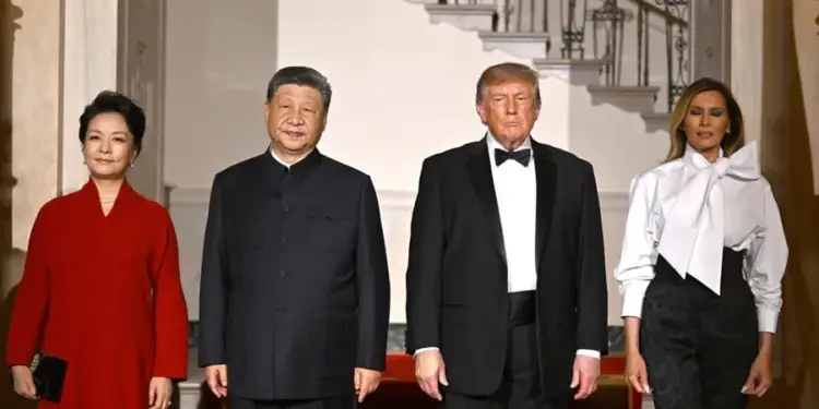Cuatro personas, dos hombres y dos mujeres, en atuendo formal posando en un evento. Un hombre lleva traje oscuro, otro esmoquin. Una mujer viste de rojo, otra de blanco y negro. Fondo con escalera.