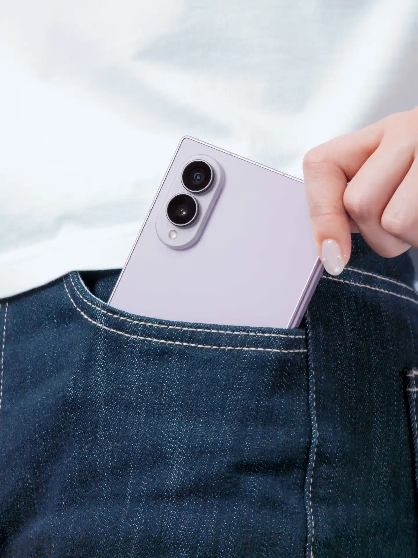 Mano de una persona guardando un smartphone violeta con doble cámara en el bolsillo trasero de unos jeans azules.