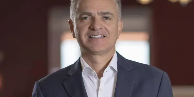 Retrato de un hombre de negocios sonriendo con chaqueta azul y camisa blanca en una oficina.