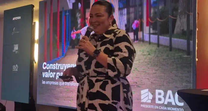 Mujer dando una conferencia empresarial frente a una pantalla con la frase Construyendo valor para las empresas.