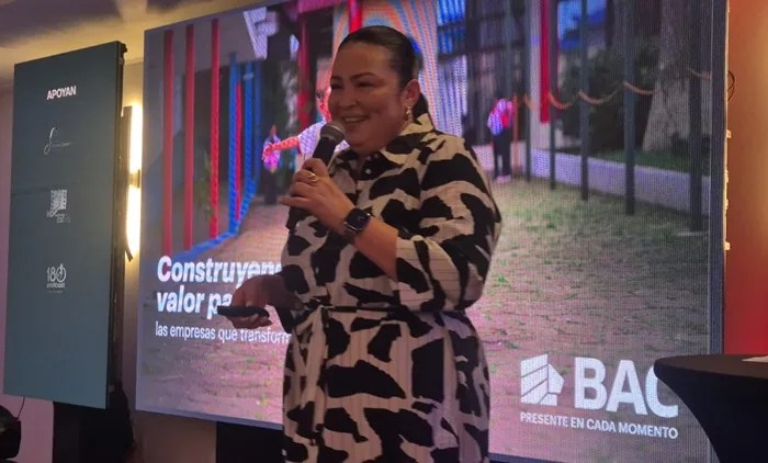 Mujer dando una conferencia empresarial frente a una pantalla con la frase Construyendo valor para las empresas.