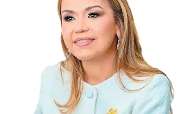 Retrato de una mujer profesional con chaqueta clara y broche dorado sobre fondo blanco