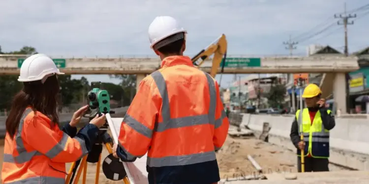 Ingenieros con cascos blancos y chalecos reflectantes usando un teodolito en una obra de construcción.