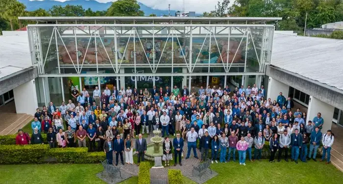 Vista aérea frontal de un numeroso grupo de profesionales posando frente a la entrada de un edificio corporativo moderno con mural