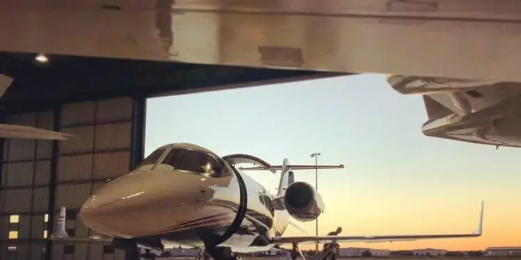 Jet privado estacionado dentro de un hangar de aviación con la puerta abierta al atardecer.