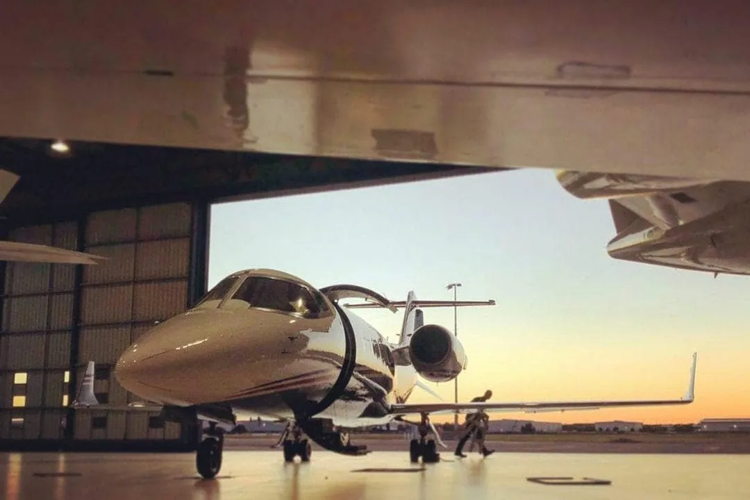 Jet privado estacionado dentro de un hangar de aviación con la puerta abierta al atardecer.