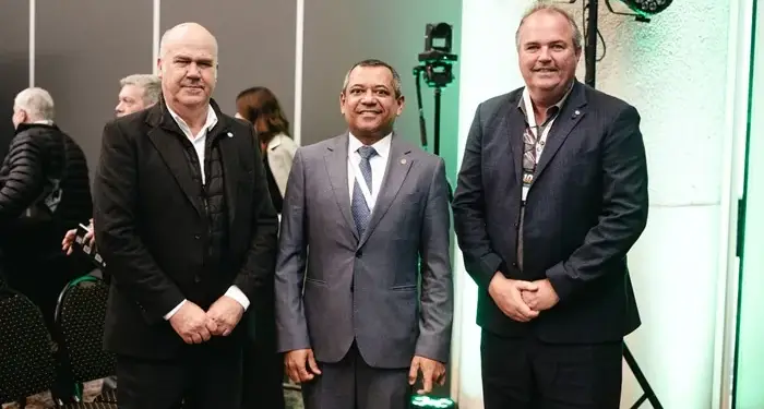 Tres hombres con traje formal posando juntos en un evento empresarial con iluminación de estudio.