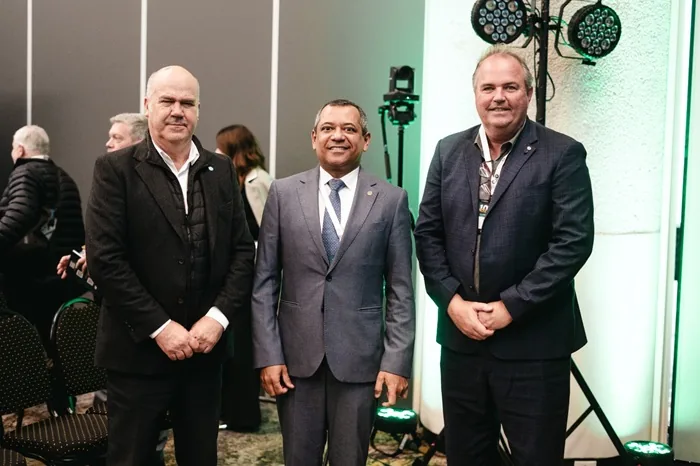Tres hombres con traje formal posando juntos en un evento empresarial con iluminación de estudio.