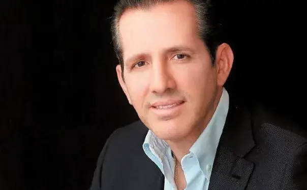 Hombre de negocios sonriendo con traje oscuro y camisa clara sobre fondo negro