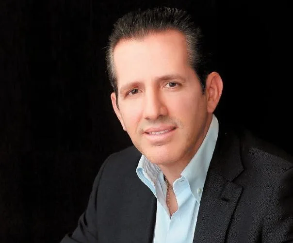 Hombre de negocios sonriendo con traje oscuro y camisa clara sobre fondo negro
