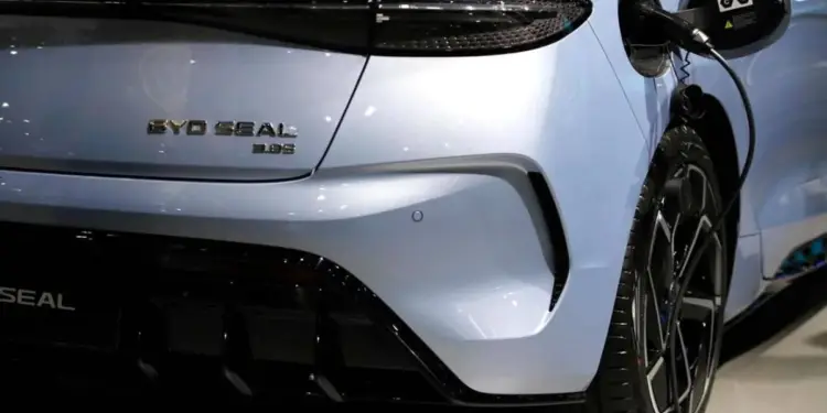 Parte trasera de un coche eléctrico BYD Seal color plata claro, conectado a un cargador. Detalle del puerto de carga y el emblema del modelo.