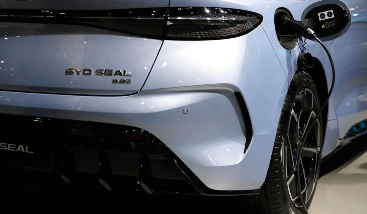 Parte trasera de un coche eléctrico BYD Seal color plata claro, conectado a un cargador. Detalle del puerto de carga y el emblema del modelo.