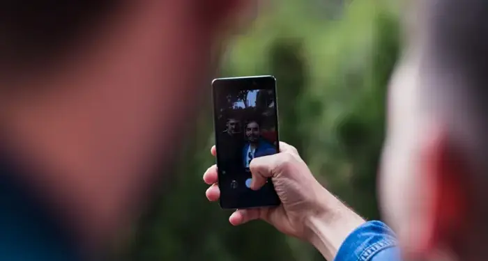Primer plano de una persona usando un teléfono móvil para tomar una fotografía al aire libre con fondo verde.