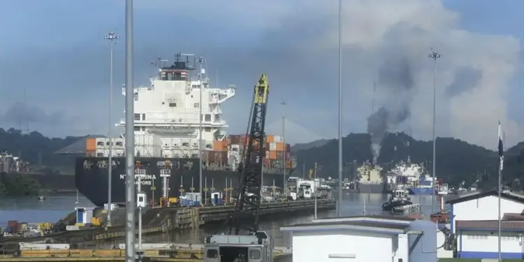 Gran buque portacontenedores con texto 'CHINA SINGAPORE' en su casco, navegando por un canal. Se ven una locomotora, grúa, humo y colinas.