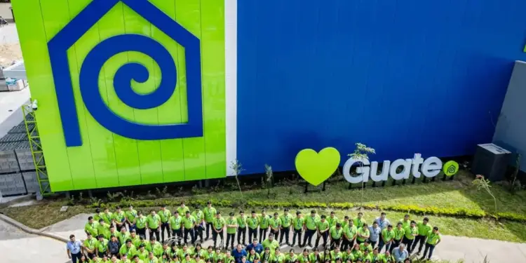 Gran grupo de empleados posando frente a la fachada azul y verde de un edificio comercial con un logotipo de una casa.