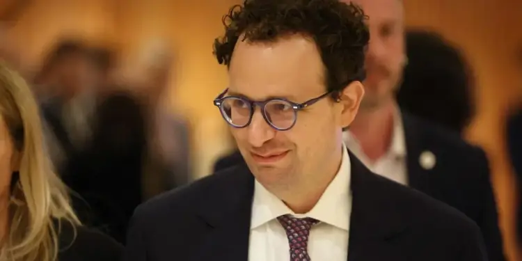 Hombre de negocios con gafas y traje oscuro sonriendo en una conferencia.