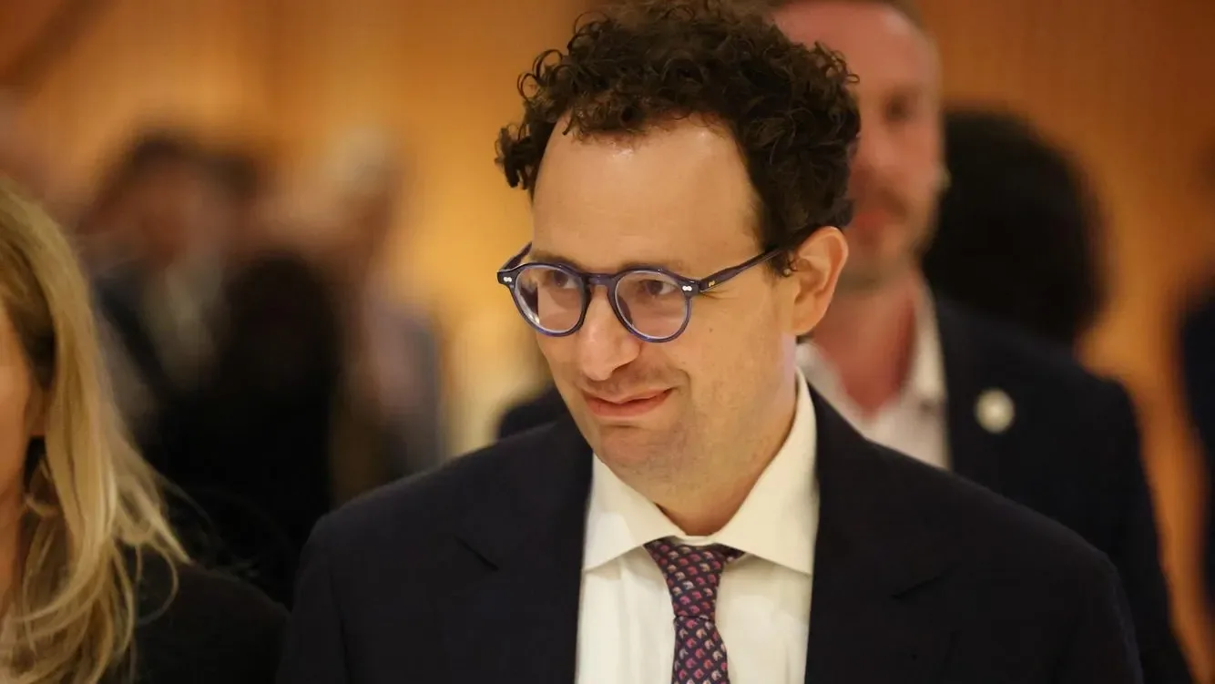 Hombre de negocios con gafas y traje oscuro sonriendo en una conferencia.