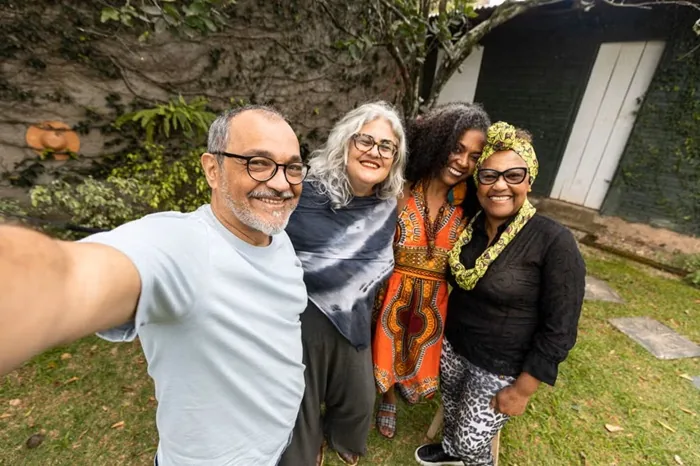 Cuatro amigos de diversas edades y etnias tomándose una autofoto sonrientes en un jardín.
