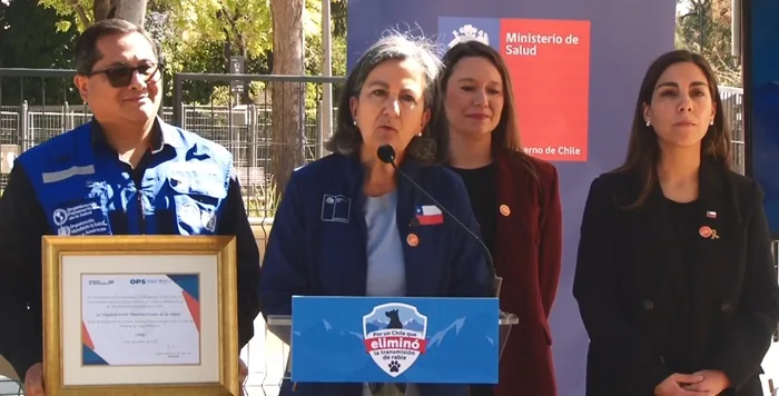 Cuatro personas en una conferencia de prensa con un cartel del Ministerio de Salud de Chile y un certificado enmarcado.