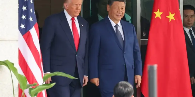 Dos líderes políticos, uno con traje azul y corbata roja junto a la bandera de EE. UU., y otro con traje azul y corbata oscura junto a la bandera de China, en un encuentro diplomático.