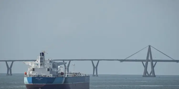 Un gran buque carguero navega por el mar con un puente colgante y atirantado de fondo bajo un cielo despejado.