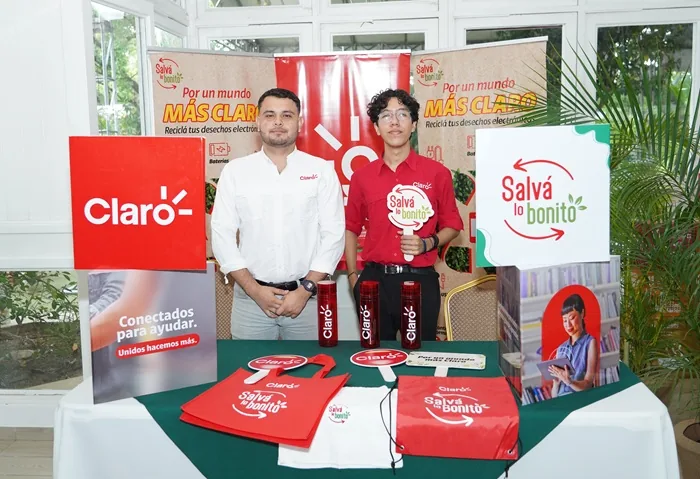 Dos hombres jóvenes posan junto a una mesa con material promocional de Claro y la campaña de reciclaje Salvá lo bonito.