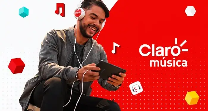 Hombre sonriente con auriculares Claro música y tablet, disfrutando contenido digital. Fondo rojo con logo Claro música y notas musicales.