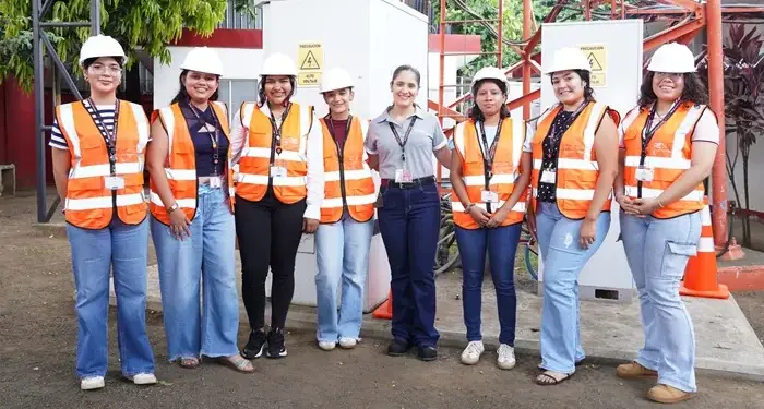 Grupo de siete mujeres profesionales con cascos blancos y chalecos reflectantes en una instalación industrial exterior.