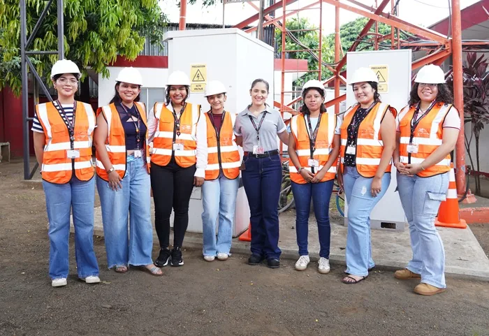 Grupo de siete mujeres profesionales con cascos blancos y chalecos reflectantes en una instalación industrial exterior.