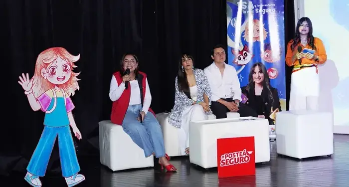 Cuatro personas sentadas en un panel de discusión en un escenario con una figura de cartón y un cartel que dice Posté Seguro.