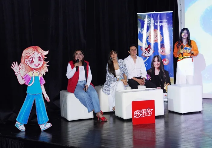 Cuatro personas sentadas en un panel de discusión en un escenario con una figura de cartón y un cartel que dice Posté Seguro.