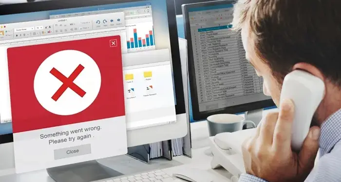 Un profesional en su oficina atiende una llamada telefónica mientras una computadora muestra un mensaje de error rojo.