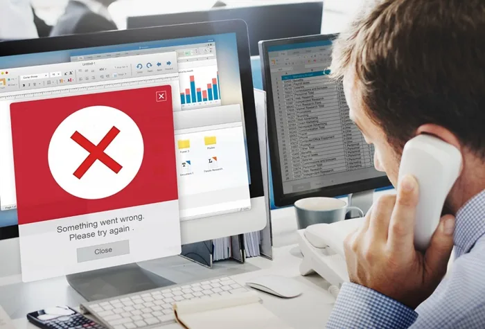Un profesional en su oficina atiende una llamada telefónica mientras una computadora muestra un mensaje de error rojo.