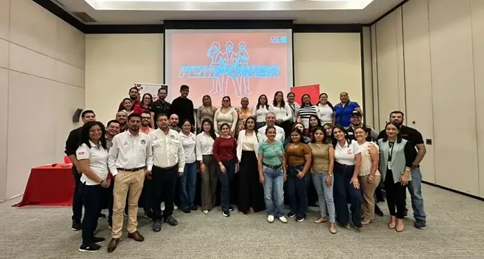 Grupo diverso de profesionales sonriendo juntos en un evento corporativo frente a una pantalla con la palabra FEMPOWER.