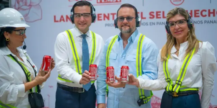 Cuatro ejecutivos con chalecos de seguridad y gafas sostienen latas rojas de refresco en un evento de Coca-Cola FEMSA.
