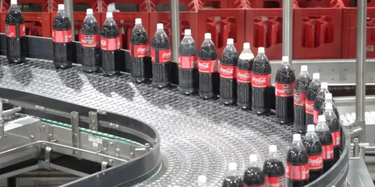 Botellas oscuras con etiquetas rojas avanzando en una cinta transportadora industrial.