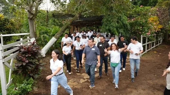 Un grupo diverso de hombres y mujeres profesionales caminan sonrientes por un sendero al aire libre rodeado de vegetación.