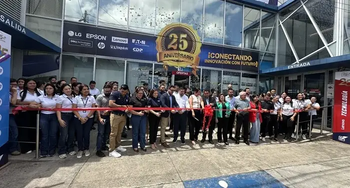 Grupo de personas cortando una cinta roja frente a un edificio comercial durante un evento de aniversario.