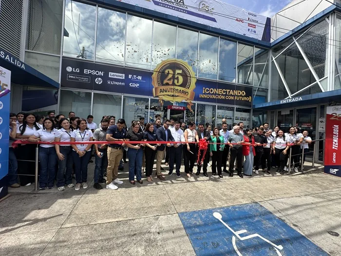 Grupo de personas cortando una cinta roja frente a un edificio comercial durante un evento de aniversario.