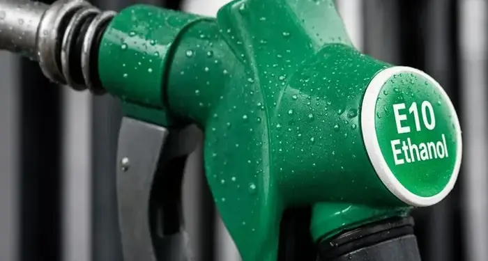 Primer plano de una pistola surtidora de combustible verde con el texto E10 Ethanol cubierta de gotas de agua.