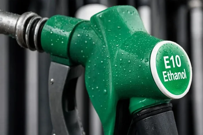 Primer plano de una pistola surtidora de combustible verde con el texto E10 Ethanol cubierta de gotas de agua.