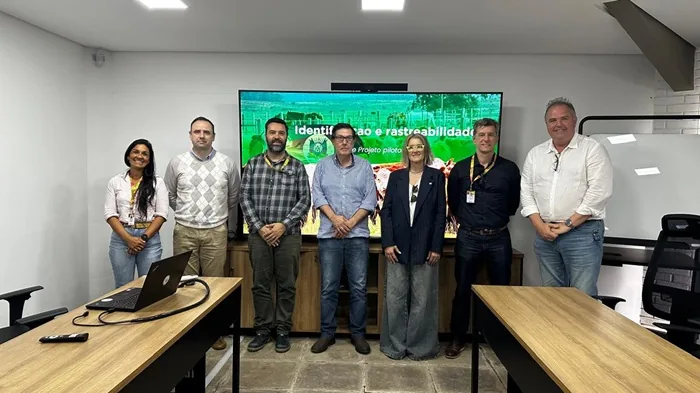 Grupo de siete profesionales en una sala de reuniones moderna. Una mujer y seis hombres posan frente a una pantalla con texto sobre identificación y trazabilidad. Mesas de madera con laptop en primer plano.