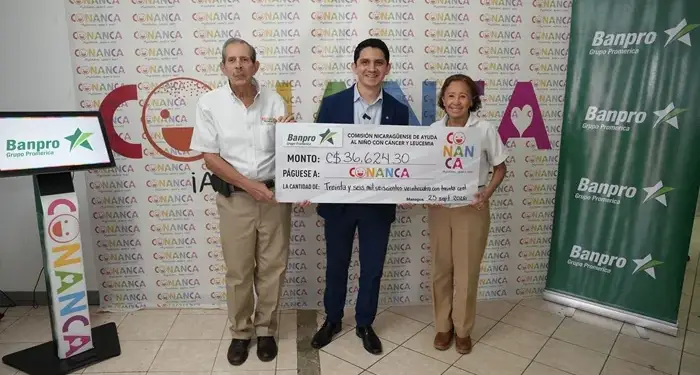 Tres personas sosteniendo un cheque simbólico grande con logotipos de Banpro y Conanca en un evento corporativo.