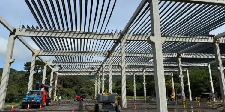 Estructura de concreto y acero en una obra de construcción industrial con maquinaria y camiones.