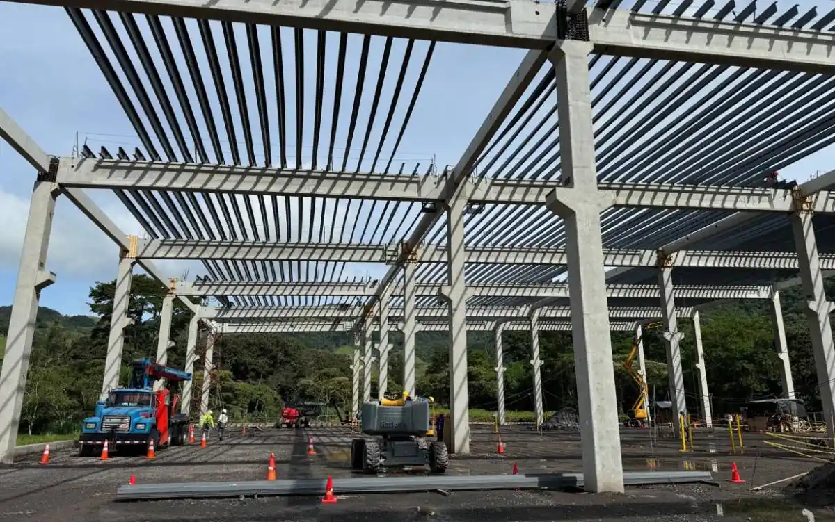 Estructura de concreto y acero en una obra de construcción industrial con maquinaria y camiones.