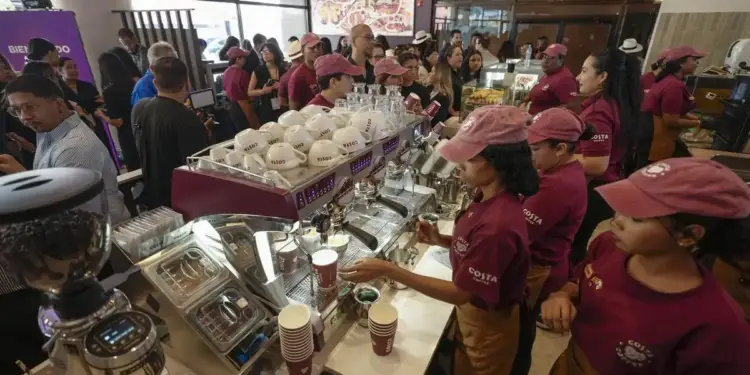 Personal con gorras y uniformes preparando café en una máquina espresso dentro de un local lleno de clientes.