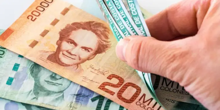 Mano contando billetes de diferentes denominaciones en colones sobre una superficie blanca.