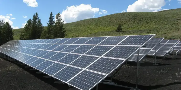 Paneles solares instalados en un campo abierto con colinas verdes y cielo nublado de fondo.
