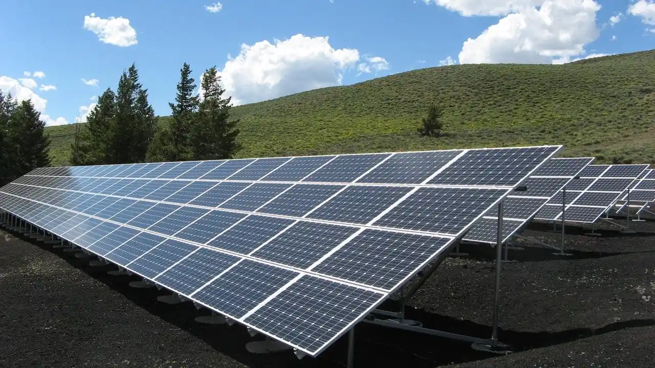 Paneles solares instalados en un campo abierto con colinas verdes y cielo nublado de fondo.